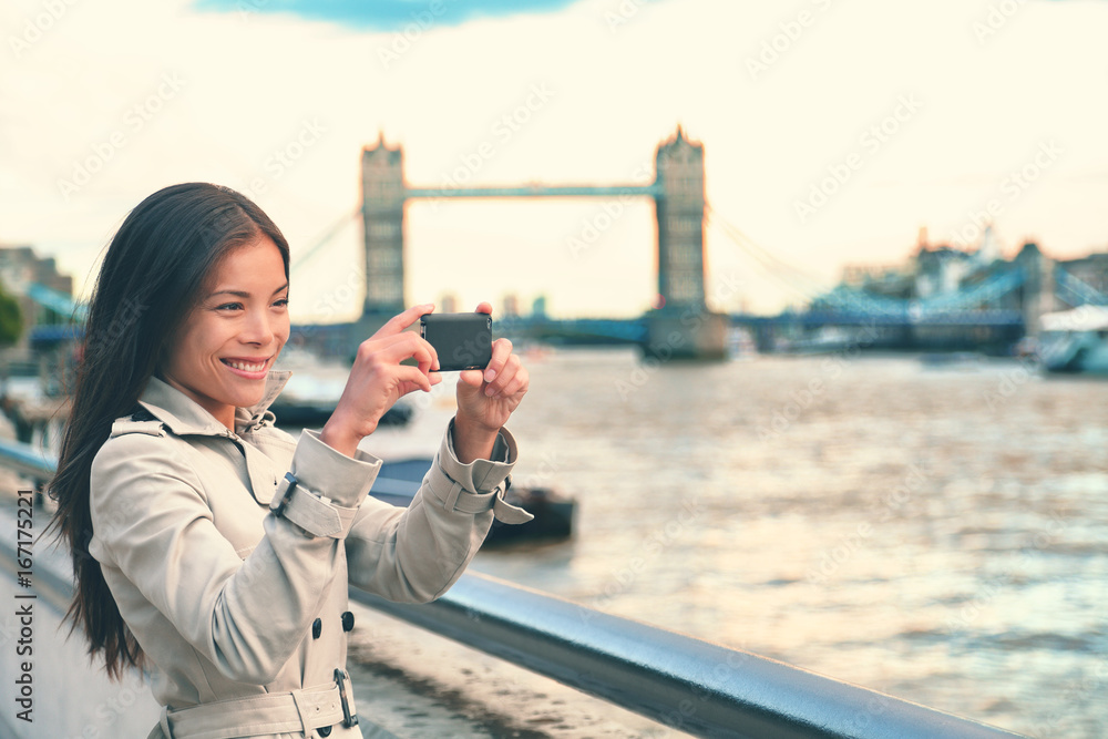 Obraz premium London woman tourist taking photo of Tower Bridge with mobile smart phone camera. Girl enjoying view over the River Thames, London, England, Great Britain. United Kingdom tourism concept.