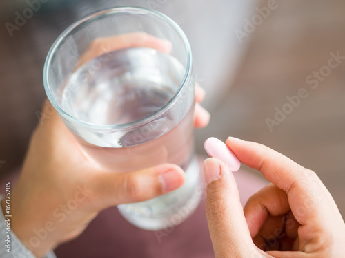 Closeup woman hand with pills medicine tablets and glass of water in her hands. Healthcare, medical supplements concept