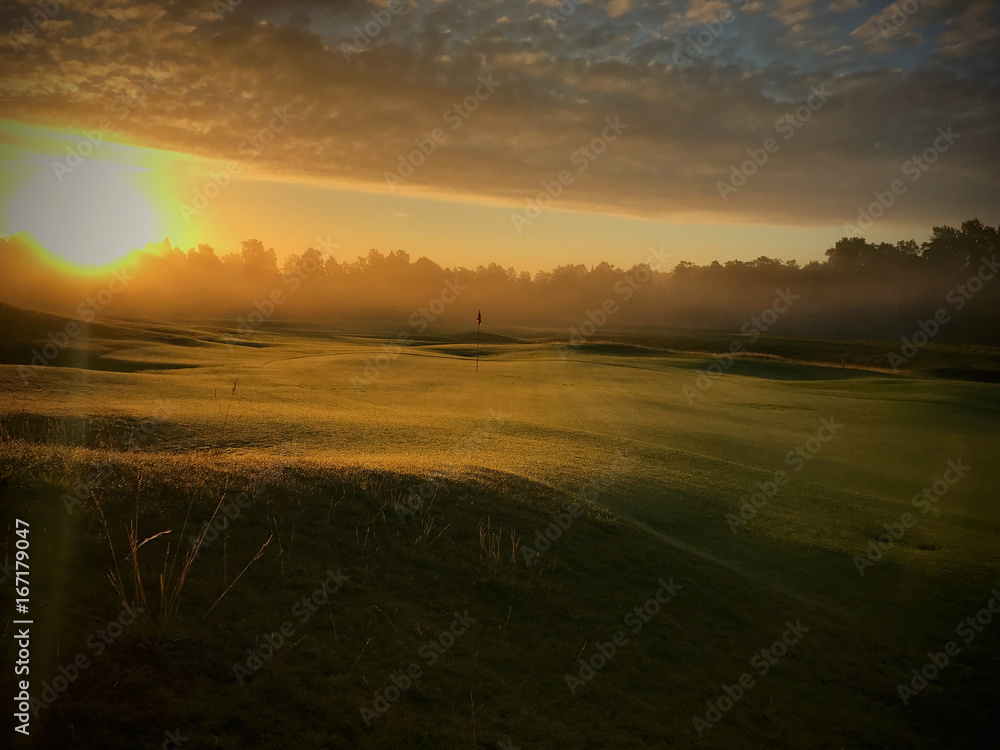 Beautiful landscape image of golf club. Sun raising up in early morning. calm and peaceful feeling. Nobody jet playing on course. Flag standing lonely with no wind.