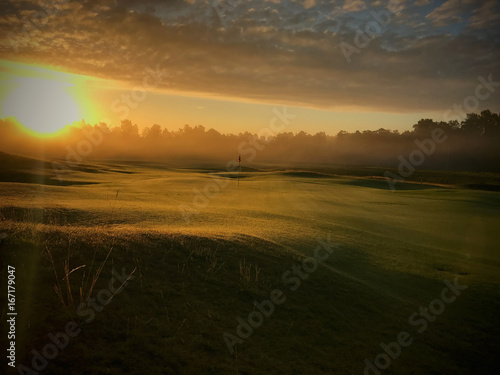 Beautiful landscape image of golf club. Sun raising up in early morning. calm and peaceful feeling. Nobody jet playing on course. Flag standing lonely with no wind.