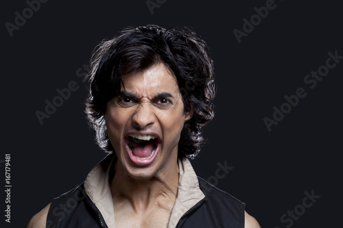 Portrait of young man screaming against black background 