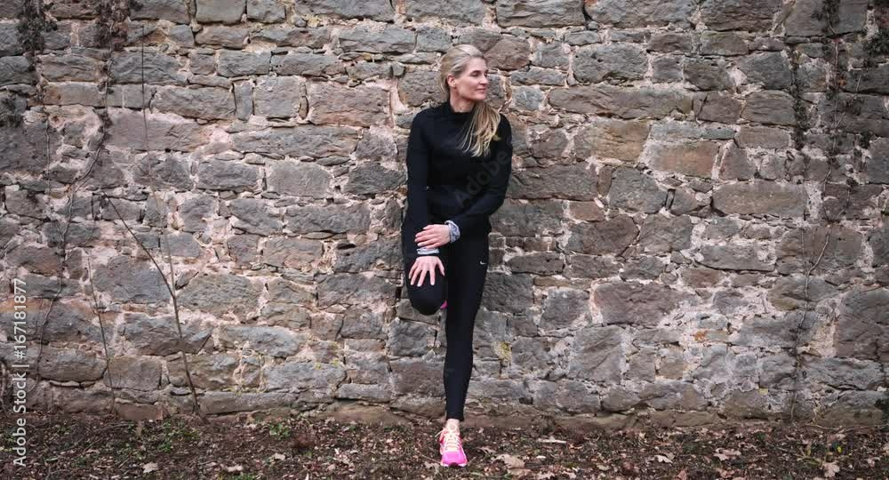 A female jogger taking a break by an ancient brick wall. She stands in one place and is filmed in long shot range. A female jogger taking a break by an ancient brick wall. She stands in one place and is filmed in long shot range.
