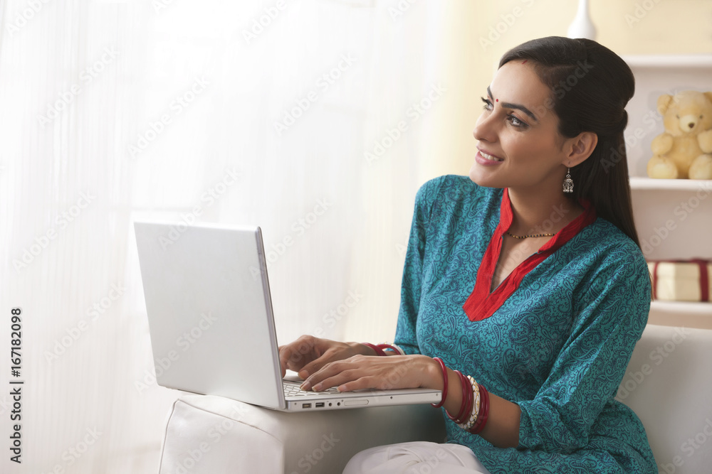 Naklejka premium Thoughtful young woman using laptop on sofa