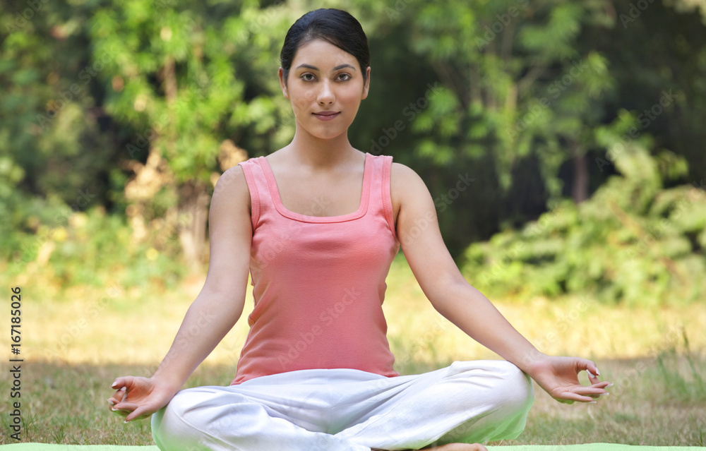 Portrait of young woman in lawn sitting in lotus position 