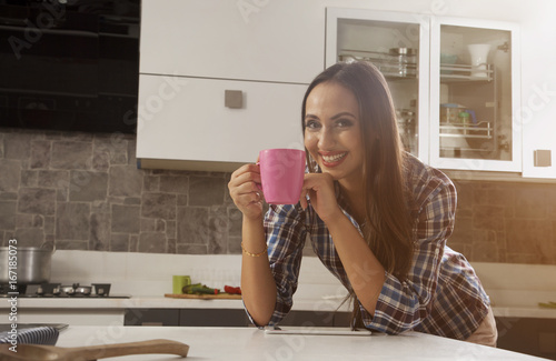 Young woman drinking coffee using digital tablet in kitchen