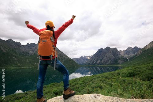 cheering young backpacking woman hiking in mountains