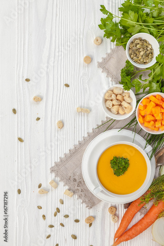 Pumpkin cream soup with croutons, raw fresh pumpkin pieces  and herbs on a white rustic wooden background
