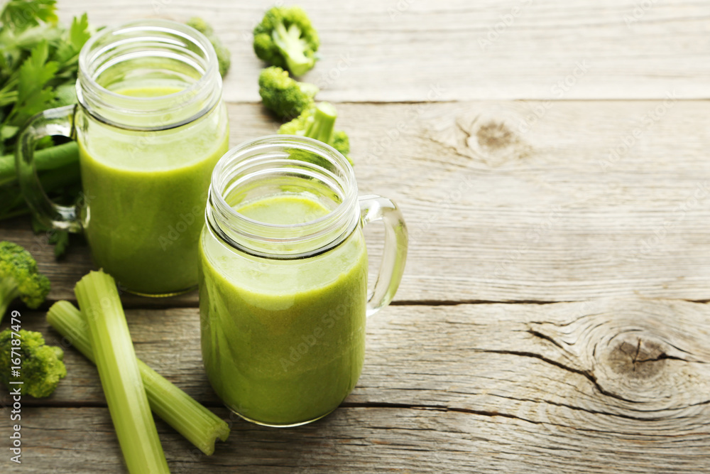 Bottles of juice with broccoli and celery on grey wooden table Bottles of juice with broccoli and celery on grey wooden table