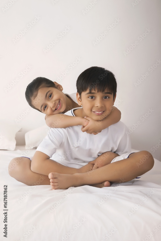 Portrait of happy girl embracing brother from behind in bed Portrait of happy girl embracing brother from behind in bed