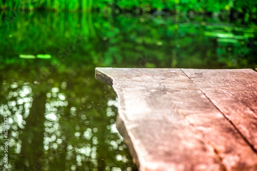 Romantic summer scene. Macro shot of wooden footbridge over the river on camping site on countryside. Abstract reflections in water. Gather thoughts and relax in nature. Peace and serenity all around.