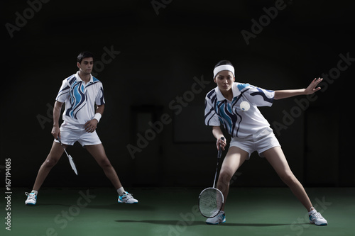 Woman hitting shuttlecock with badminton racket with partner looking at her