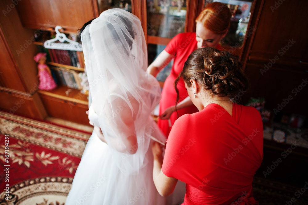 Obraz premium Helpful bridesmaids helping bride to dress up and get ready for her wedding.