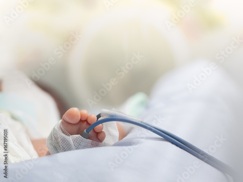 Infant or newborn baby feet with pulse oximeter for determine oxygen saturation in baby's blood, in incubator at intensive room care in the hospital after delivery photo