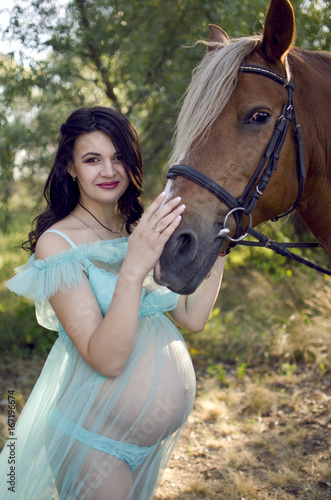 Pregnant girl in mint dress. Pregnant woman with horse. Motherhood