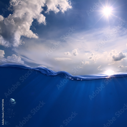 Aquatic Marine Scenery With Bright sun on the sky. White clouds. Ocean Wave divided by waterline.  Air bubbles and sun rays underwater
