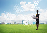 Camera headed woman standing on green grass against modern cityscape