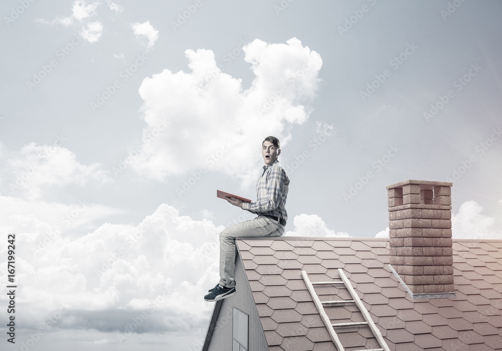 Handsome man on brick roof against cloud scape reading book Handsome man on brick roof against cloud scape reading book