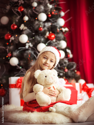 Lovely girl sitting on the floor near the Christmas tree with a bear, studio shot, toning in vintage style. © murika