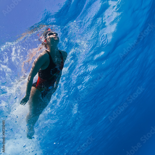 Professional female swimming in blue with air bubbles under water surface