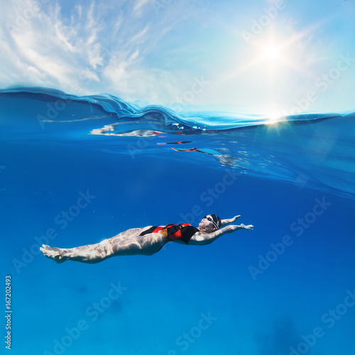 Female professional swimmer swimming on back under waterline with sunshine above