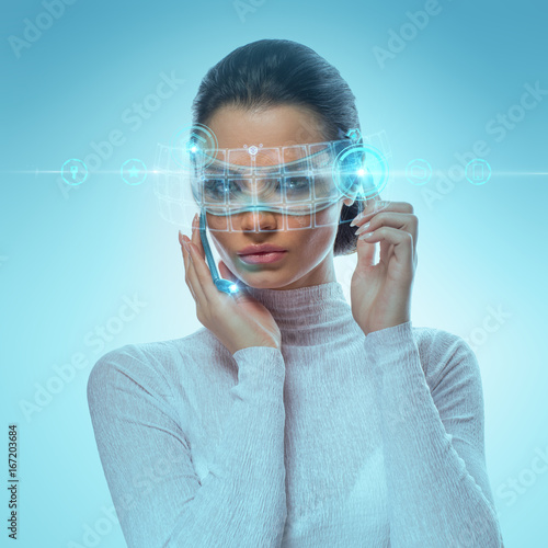 Image of Futuristic Attractive Businesswoman Wearing virtual Glasses Working With Holographic Hud Against Hightech background