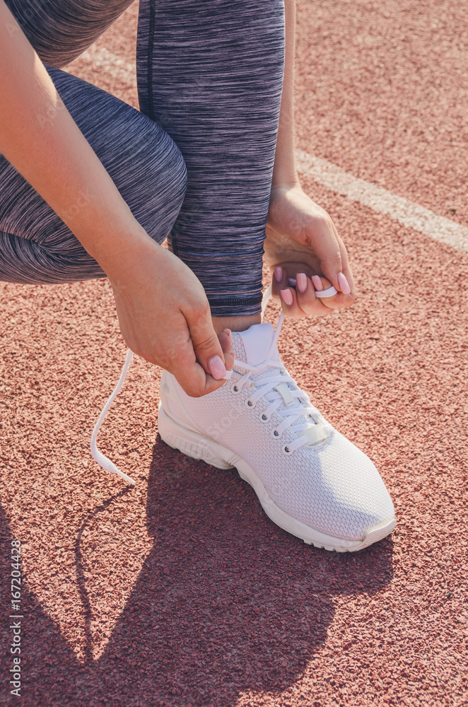 Sport girl workout. Exercise. Fitness. Health. Young girl tying her shoelaces at stadium do some training.