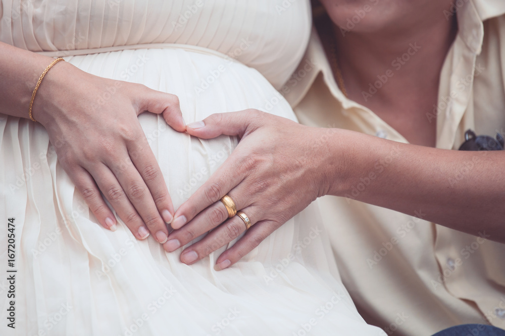 Pregnant woman and her husband making hand heart shape together on the tummy, lovely family Pregnant woman and her husband making hand heart shape together on the tummy, lovely family