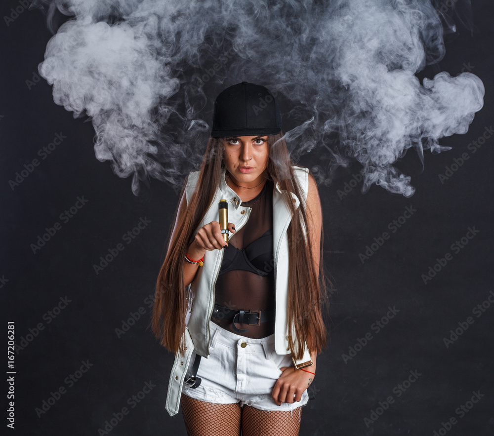 Young and very attractive woman is vaping an e-cigarette. Studio shooting.