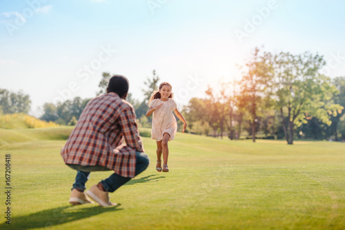 happy african american granddaughter running to grandfather on green lawn in park