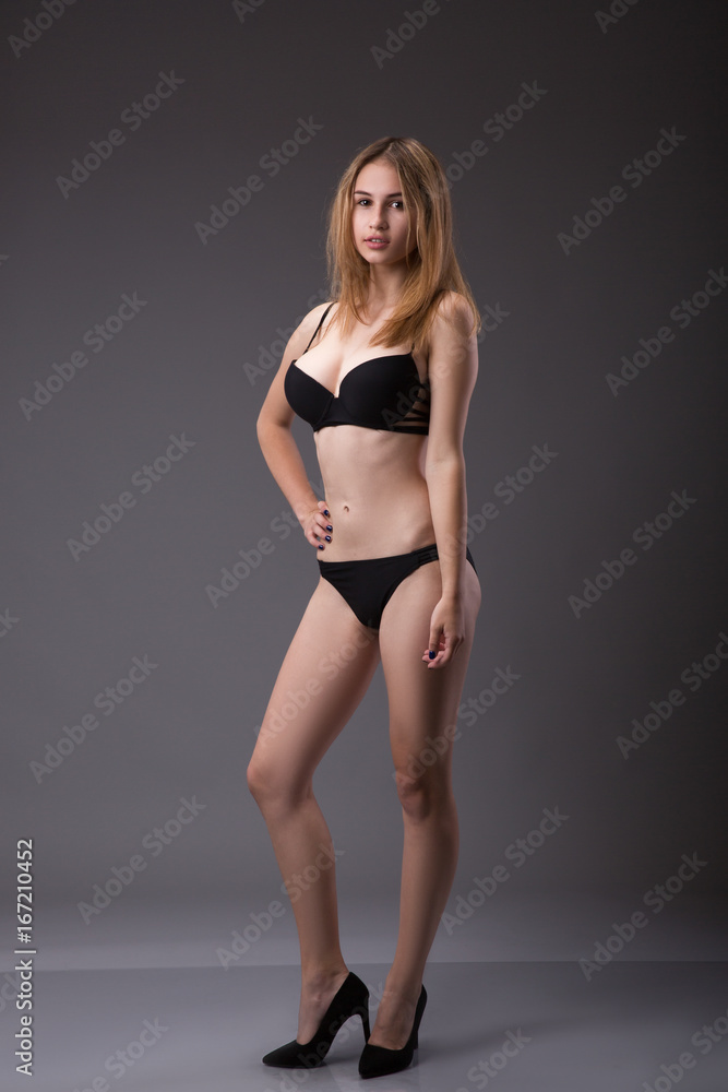 Awesome fit woman in a black lingerie or underwear posing on gray background in a studio.