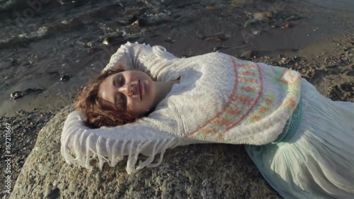 Red-haired girl is lying on a large rock on the beach.