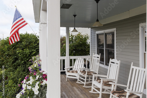USA, Bangor, Maine. A row of traditional white rocking chairs at the porch of an inn with a stars and stripes flag.