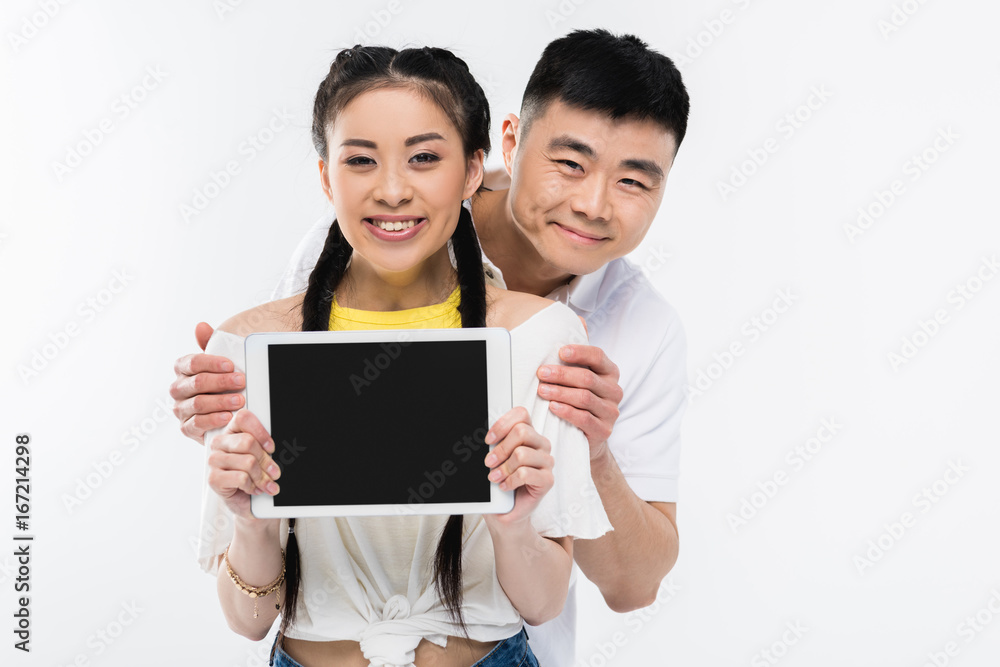 happy young asian couple showing digital tablet with blank screen and smiling at camera isolated on white happy young asian couple showing digital tablet with blank screen and smiling at camera isolated on white