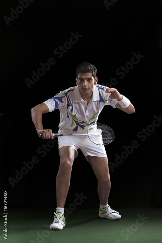Young male badminton player preparing to serve against black background