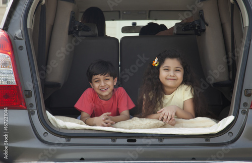 Brother and sister leaning in open boot of car 