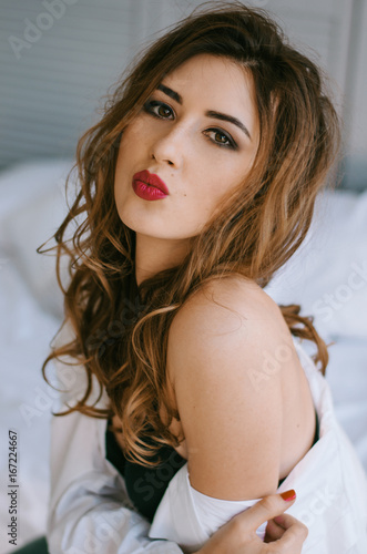 Portrait of a young woman in a black short top and white shirt, she sits on the bed photo