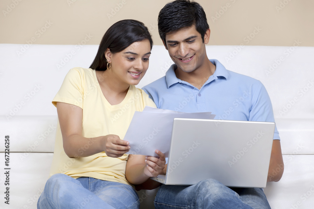 Young Indian couple reading document while using laptop Young Indian couple reading document while using laptop