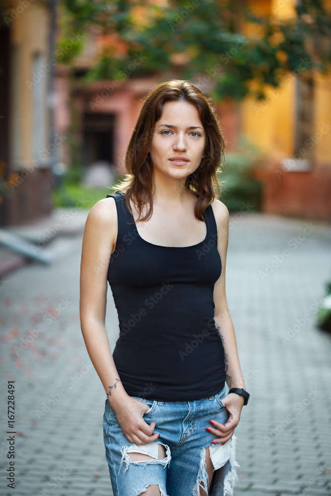 Portrait of a woman in a black T-shirt and jeans standing in the courtyard of an old house
