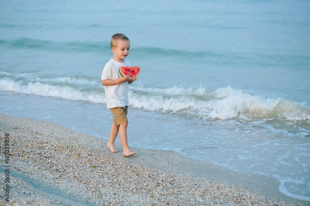 Happy child on the beach and eating watermelon outdoors