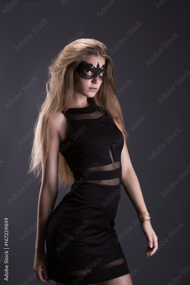 Young woman in black lace mask on the eyes. Black dress, loose hair. The dark background Young woman in black lace mask on the eyes. Black dress, loose hair. The dark background