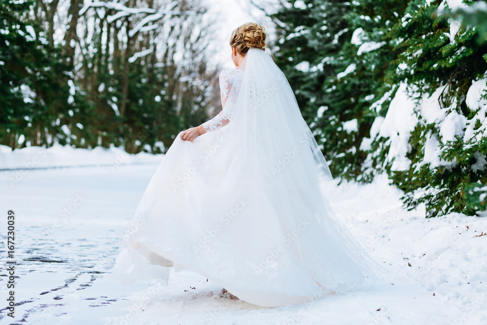 Beautiful bride running in the snowy forest, waving her dress on a wedding day. Back view. Winter ceremony
