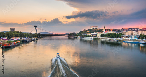 Photography Cityscape of Bratislava, Slovakia at Sunset  as Seen from a Bridge over Danube River with Motorboat Towards Old Town of Bratislava