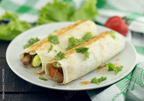 Lavash rolls with meat, vegetables and cheese served with green lettuce salad on rustic wooden table. Healthy breakfast concept. Greek traditional food - Gyro
