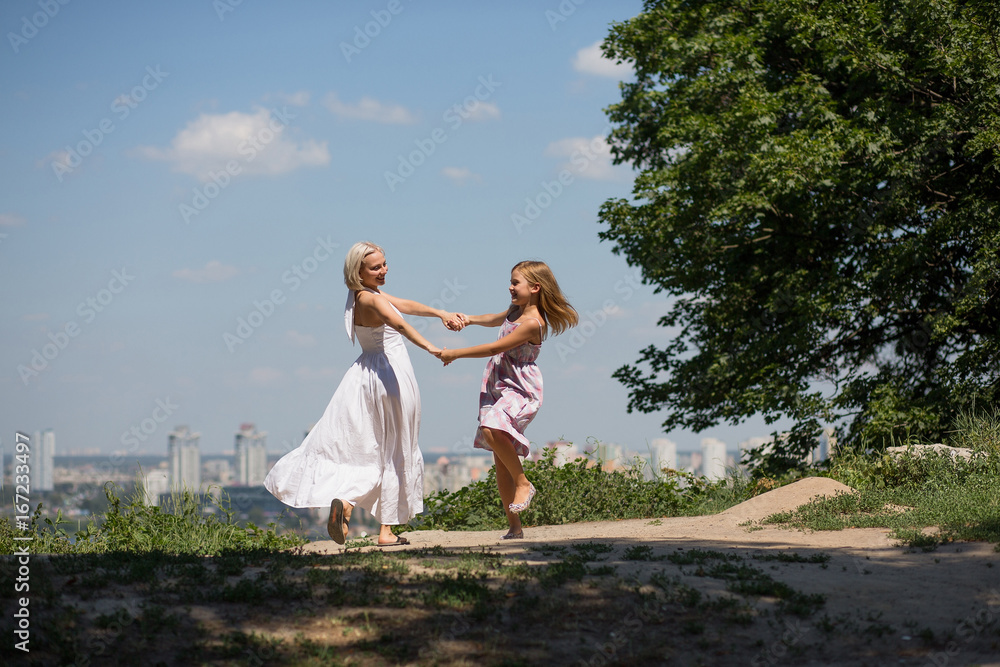 Mommy and little daughter dancing in the city park. View of happy young woman having fun with her daughter outdoors. Mommy and little daughter dancing in the city park. View of happy young woman having fun with her daughter outdoors.