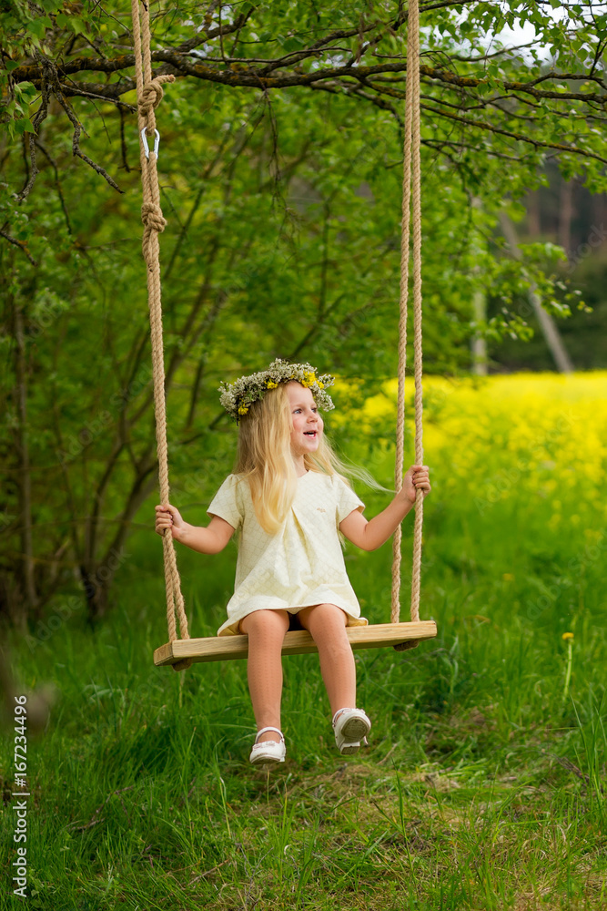 Beautiful little girl with a wreath on her head playing in a flowering field.