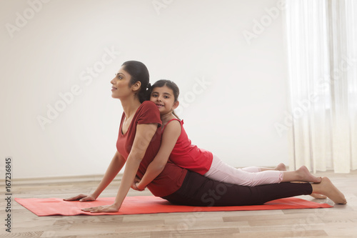 Mother practicing yoga with toddler daughter on top of her