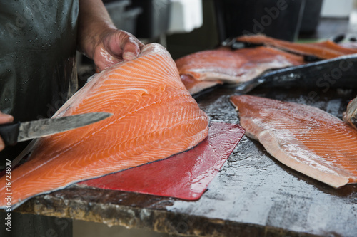 Fishmonger hands cutting whole salmon fish into big fillets