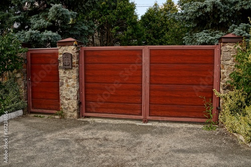 Красные деревянные ворота и закрытая калитка на каменном заборе с почтовым ящиком