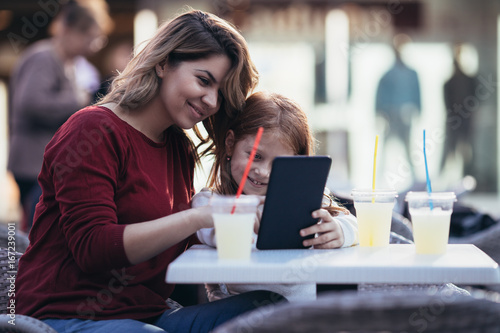 Mother and daughter sitting at cafe bar and looking something together at tablet.