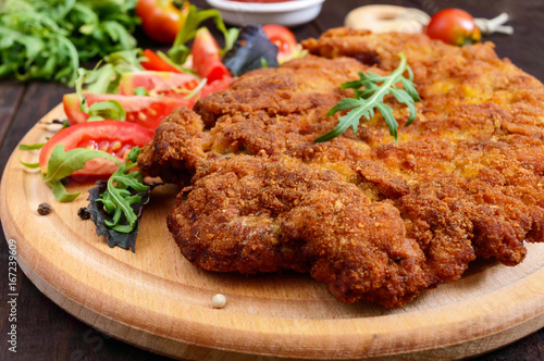 Foto A large Viennese schnitzel  and tomato salad on a cutting board on a dark wooden background